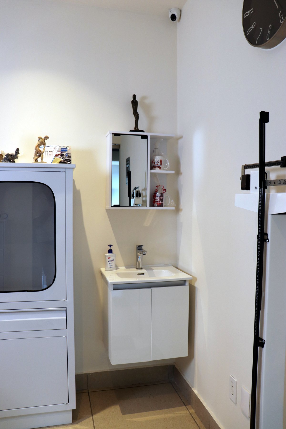 Consultorio de valoración con báscula de columna, lavabo y vitrina de instrumental.